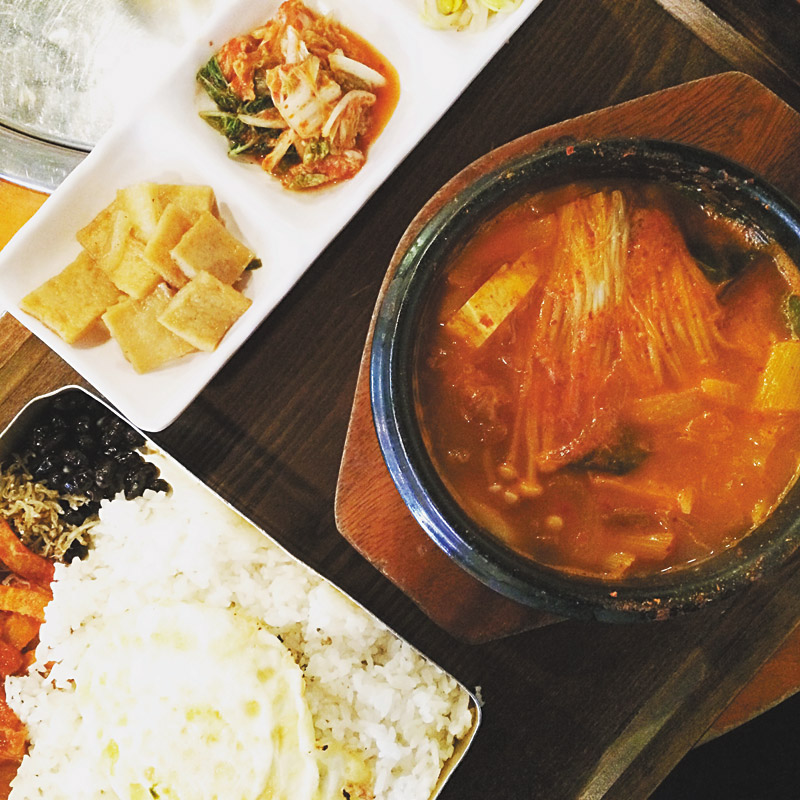 Kimchi jjigae (stew) accompanied with an old fashioned lunch box and sides 